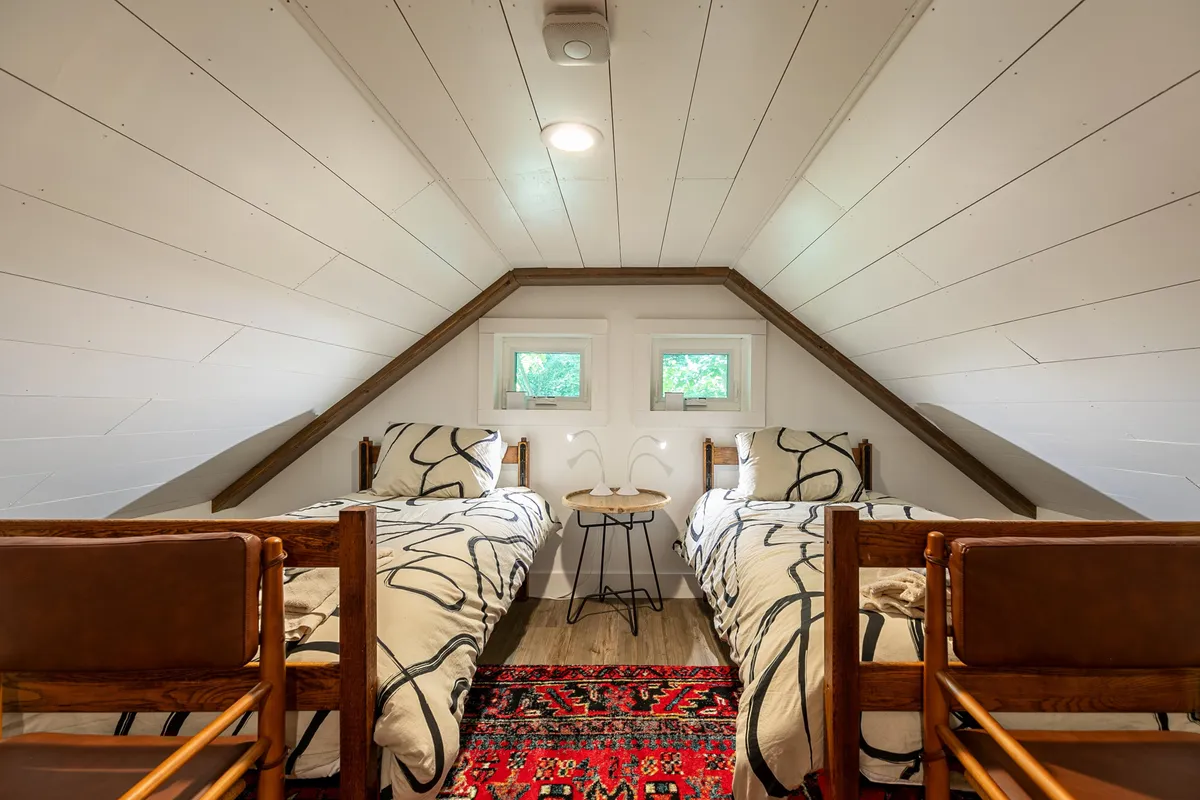 A cheerful bedroom with two twin beds, colorful decorative rug, and a small side table with decorative accents. The room is bright and inviting, ideal for children or friends traveling together.