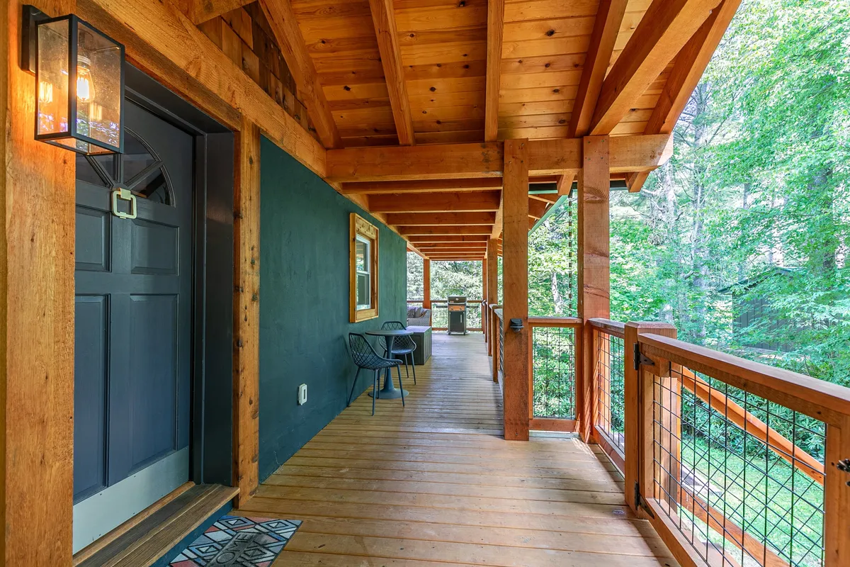 The front entrance of the property with a wooden railing, outdoor seating, and trees all around. The scene feels peaceful and welcoming, suggesting a natural transition between outdoor adventures and the comforts of home.