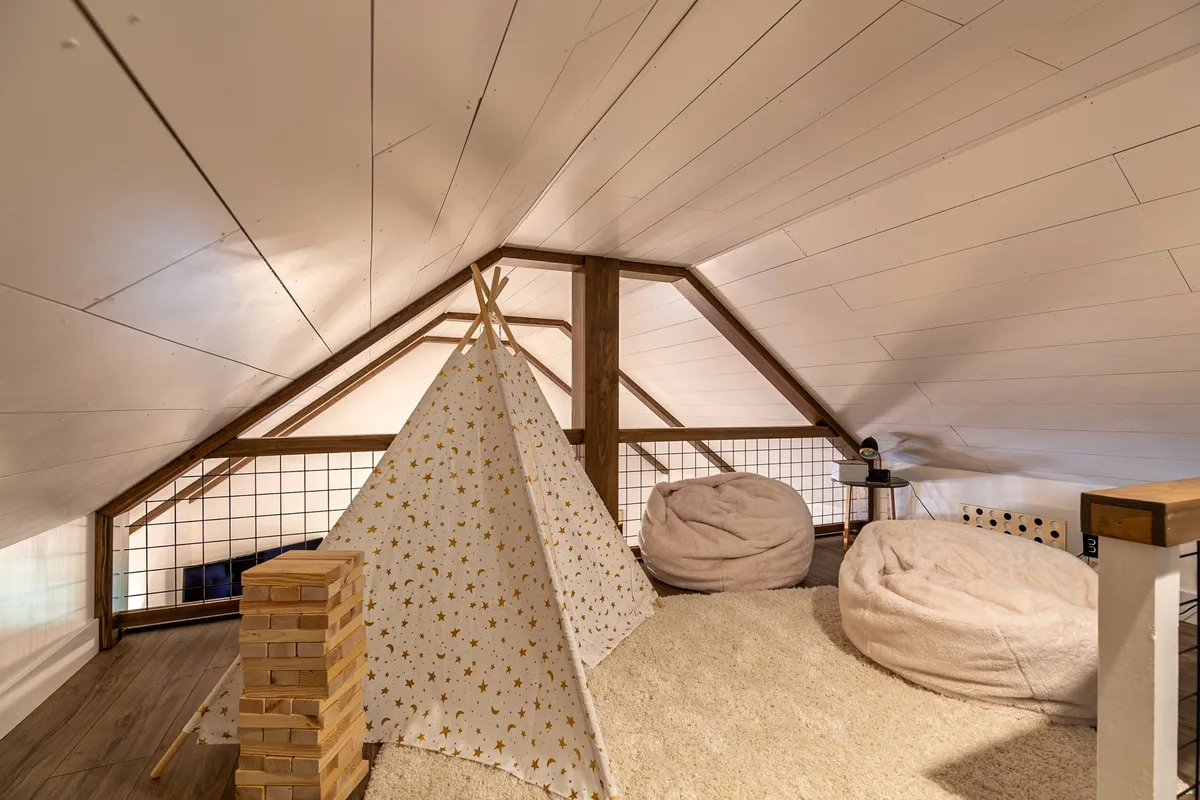 A playful loft area featuring a teepee tent, bean bag chairs, and a stack of wooden blocks. The atmosphere is whimsical and inviting, creating an imaginative play space for children.