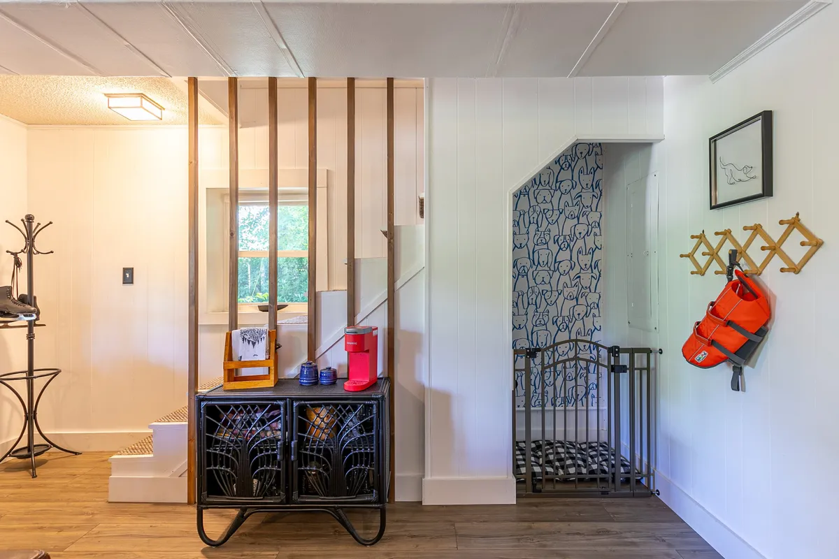 A functional and inviting interior entry area featuring a staircase, decorative storage, wall art, and a kid’s safety gate, ideal for storing outdoor gear and making an easy transition from adventures to home life.