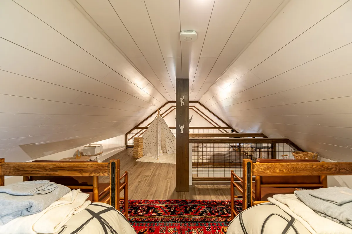A playful loft area featuring wooden beds, a colorful rug, and a whimsical teepee play area under exposed wooden beams. The space is bright, open, and inviting—ideal for older children or imaginative play.