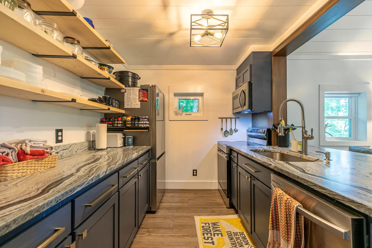 A cozy, functional kitchen scene with granite countertops, open shelving, modern appliances, and a window over the sink. The space suggests warmth and practicality, ideal for preparing meals and enjoying casual gatherings.
