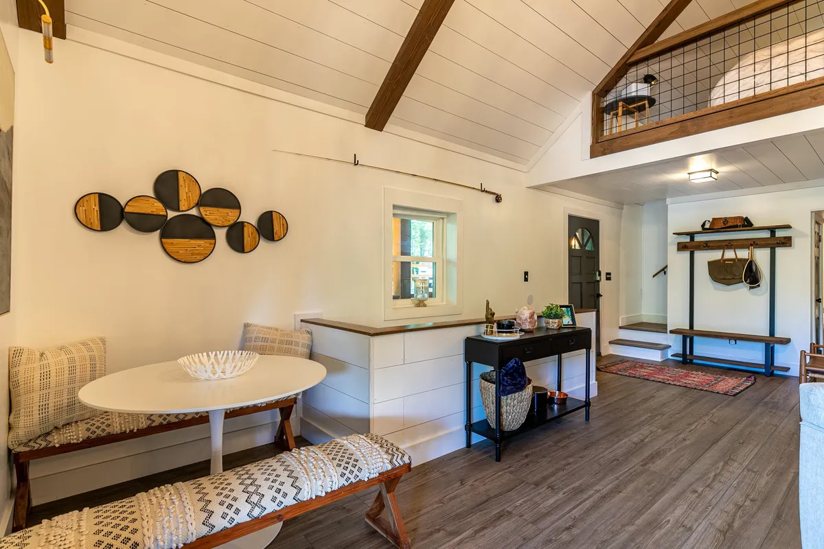 An inviting dining nook featuring a round table, bench seating, decorative wall art, and an open staircase. The space is designed for shared meals and lively conversation.