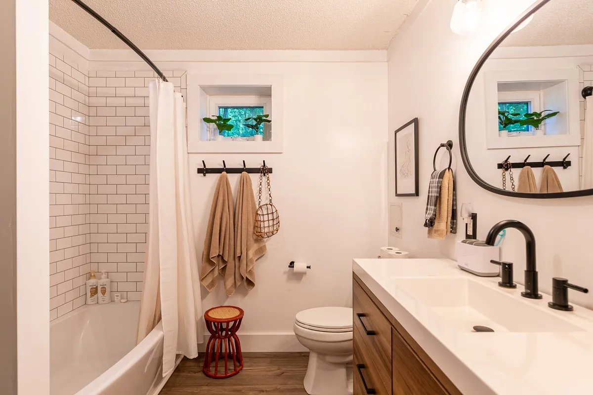 A calm, inviting bathroom with a vanity and sink, bathtub, small red stool, and towels neatly arranged on a rack. The space feels spa-like and is clearly designed for relaxation and rejuvenation.